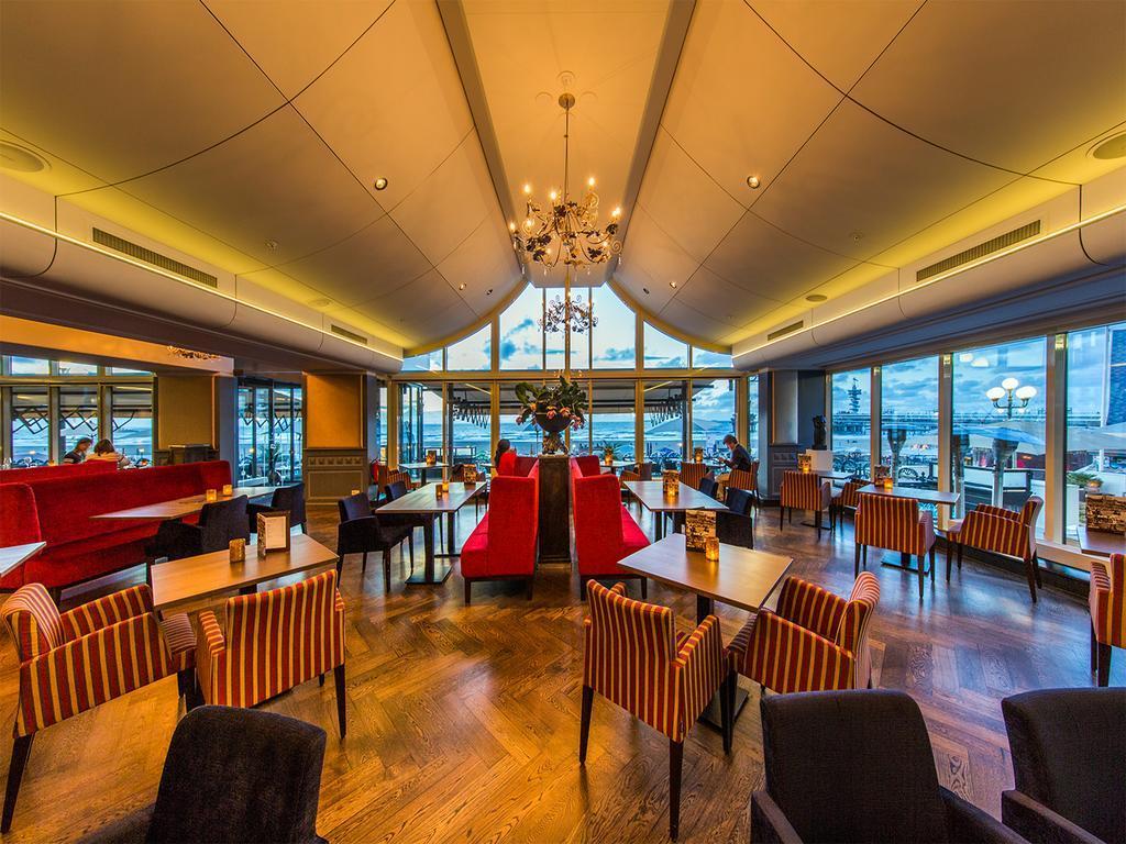 Grand Hotel Amrath Kurhaus The Hague Scheveningen Экстерьер фото The photo shows the interior of a stylish restaurant or café. It features a modern design with a high ceiling and large windows that allow natural light to fill the space. The seating includes a mix of plush red armchairs and striped chairs around wo